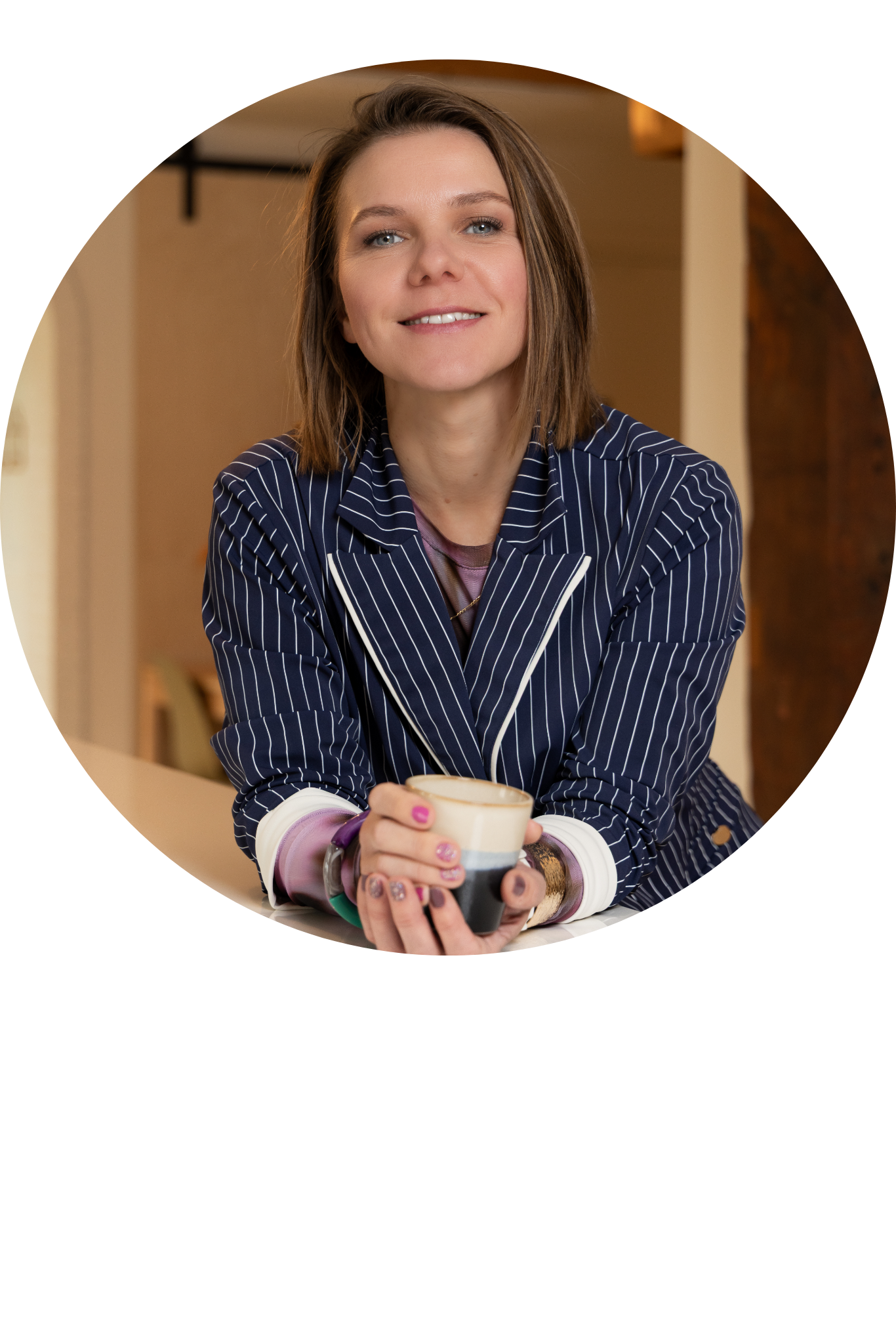 Smiling woman in a navy pinstripe blazer holding a mug at a table, circular crop.